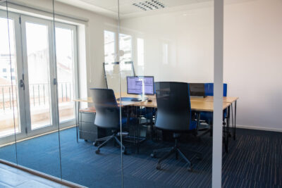 empty boardroom glass wall meeting room with conference table shared desk team workplaces trading graphs monitor office interior commercial real estate concept